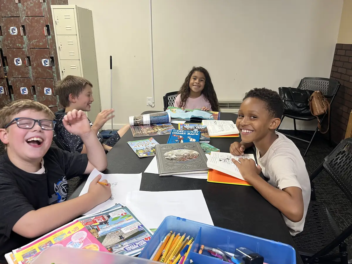 Four kids laughing round the AfterSchool homework table with books and pencils out