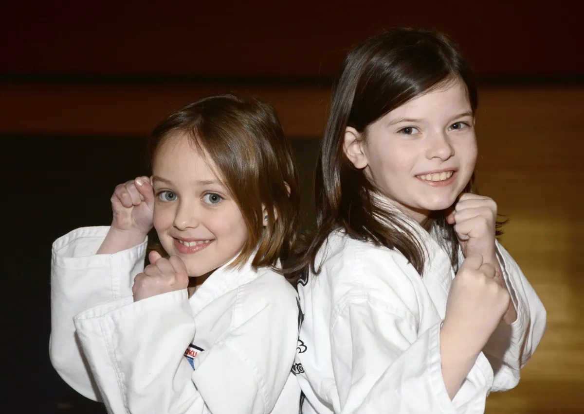 Two young girls in white gis grinning with their fists up in a fighting stance