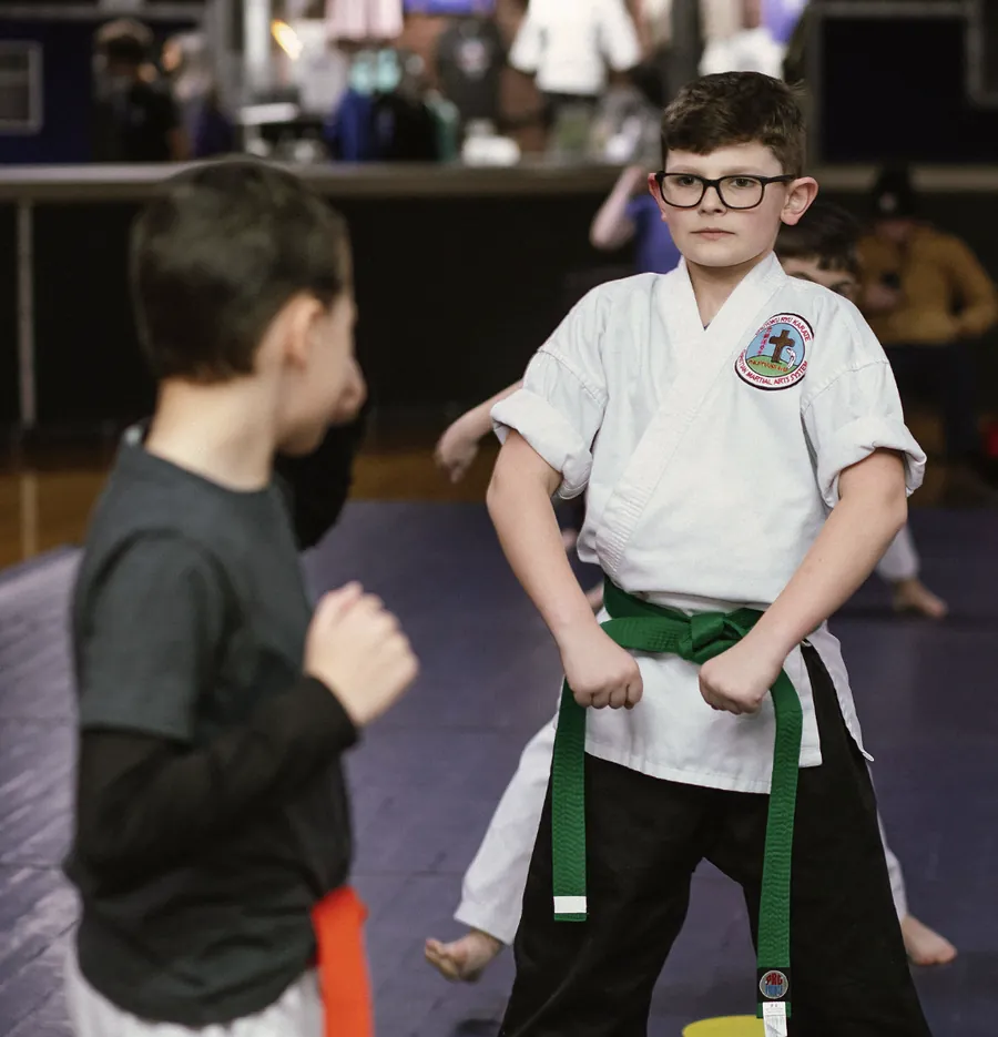A young green-belt student in a white gi standing ready in class, focused and looking straight ahead