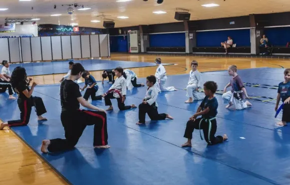 A kids' karate class stretching in rows on the blue mats at the Virginia Beach location, an instructor leading from the front